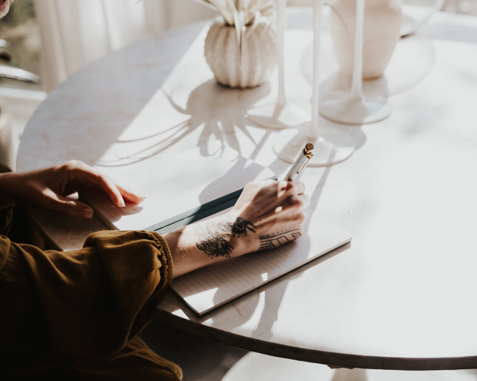 Branding Photographer,  a  woman writes in her journal at the table, tattoos on her hands