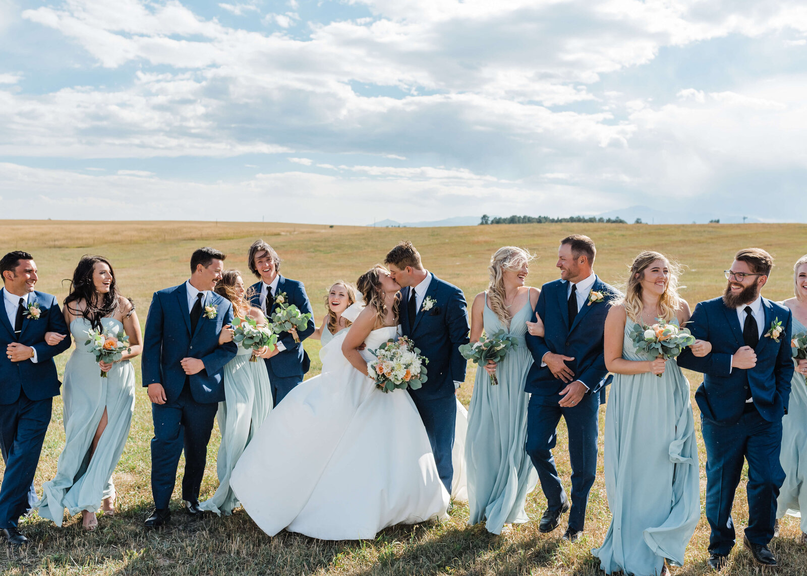 A large bridal party walk together and laugh in an open field after the wedding ceremony of their best friends