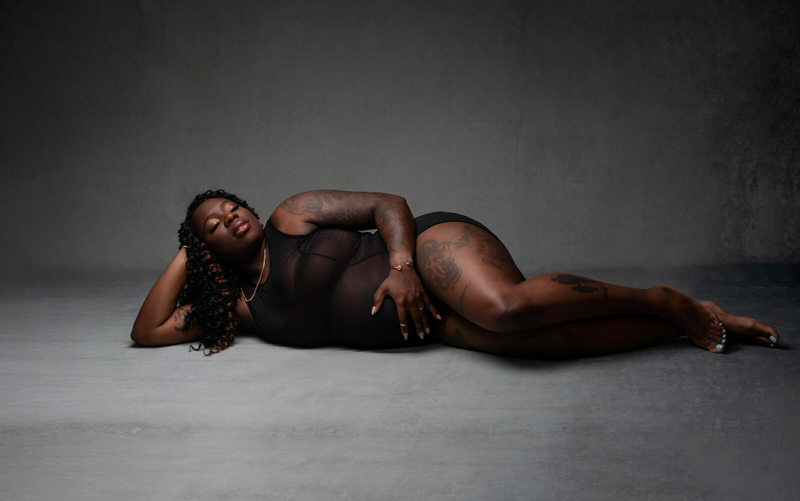 Mom laying down embracing belly in photographer wardrobe.
