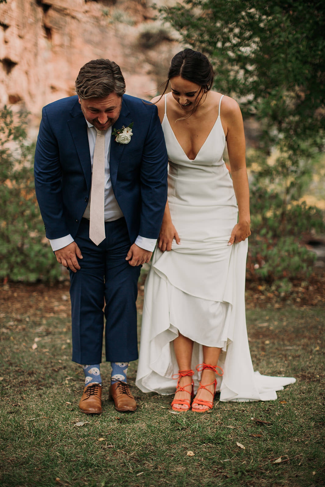 A bride and groom standing next to each other as they lift up their outfits to show off their shoes.