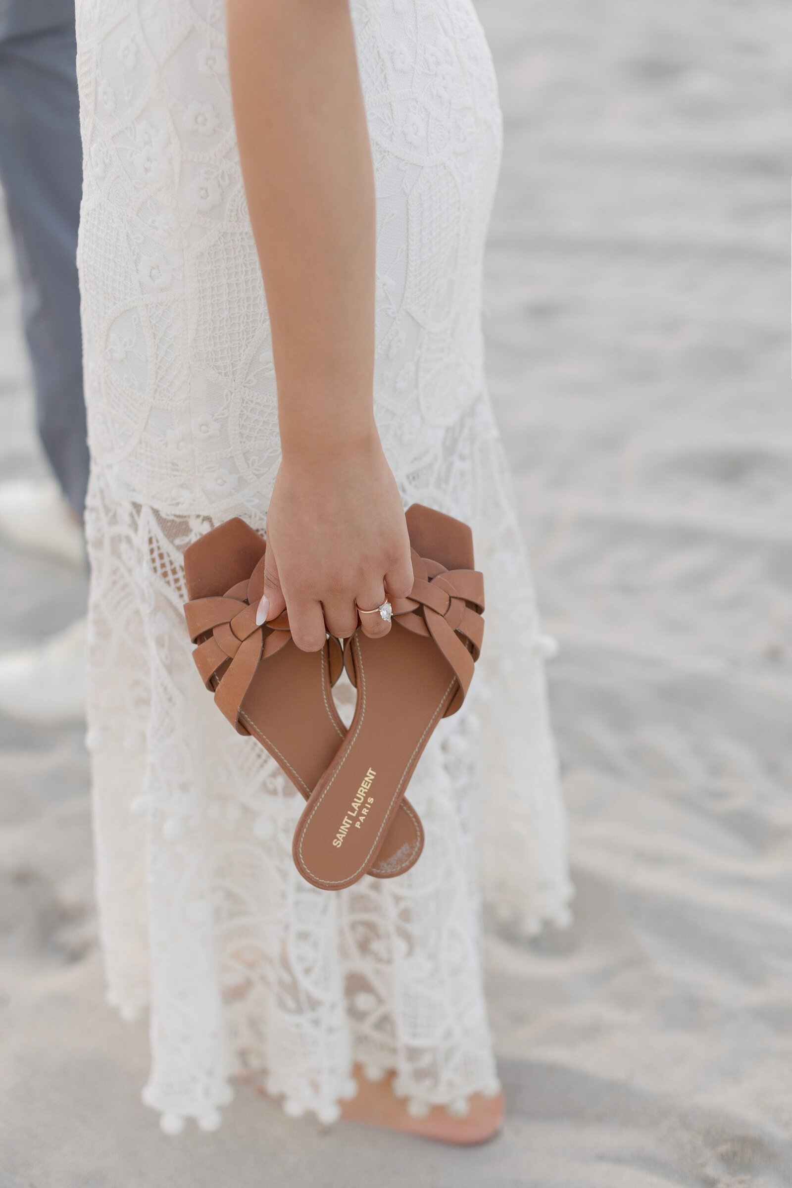 Close up images of woman holding a pair of brown Saint Laurent sandals against lace dress.