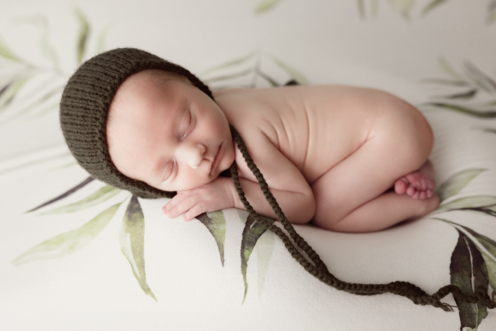 Newborn boy in a green bonnet sleeping curled up