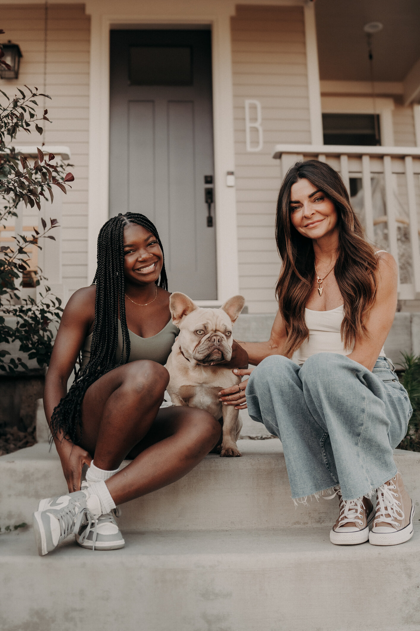 A biracial mom and daughter sit on the steps of their front porch with their adorable puppy in between them at sunrise.