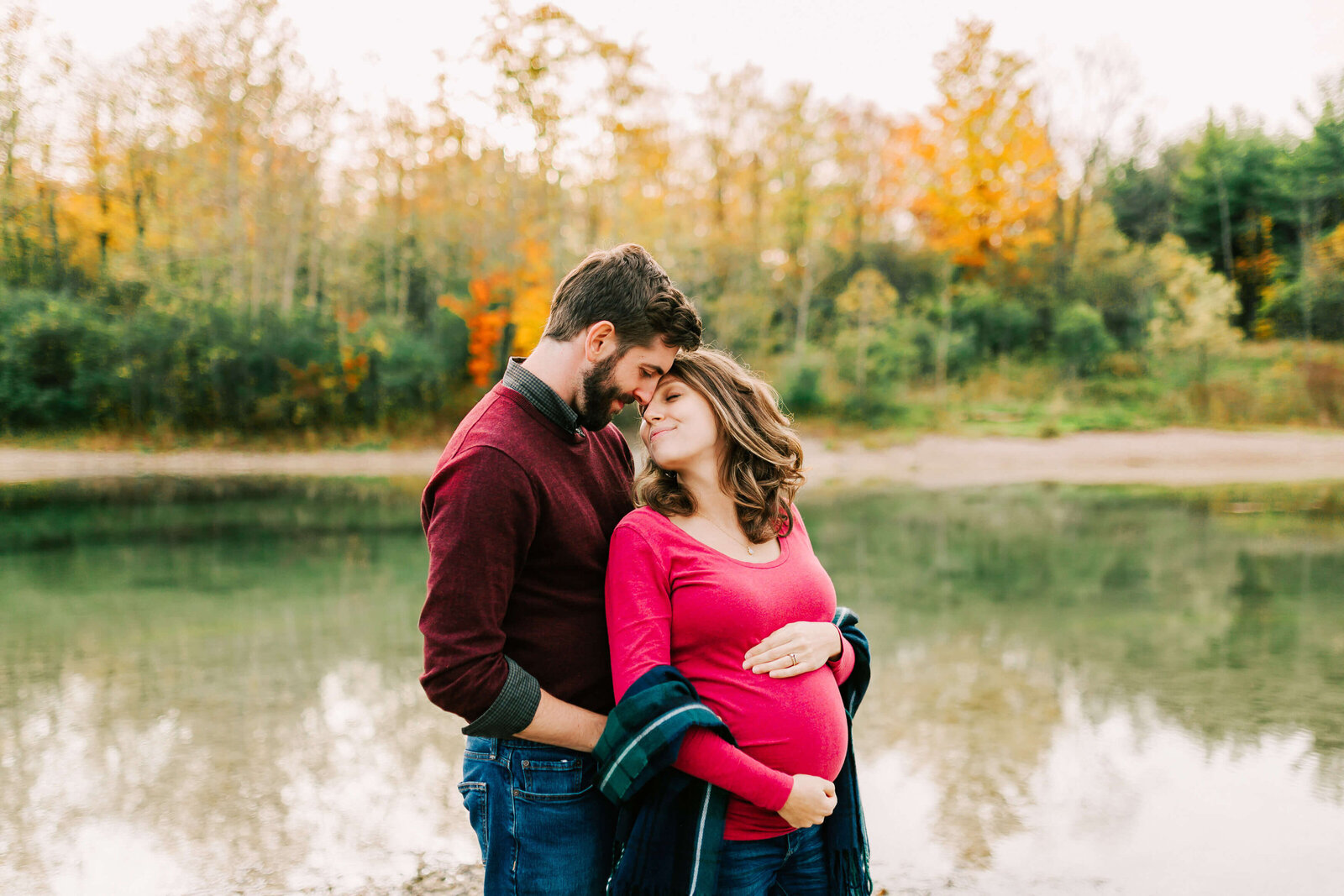 A sweet expecting couple embrace in front of the water at Puslinch Tract.
