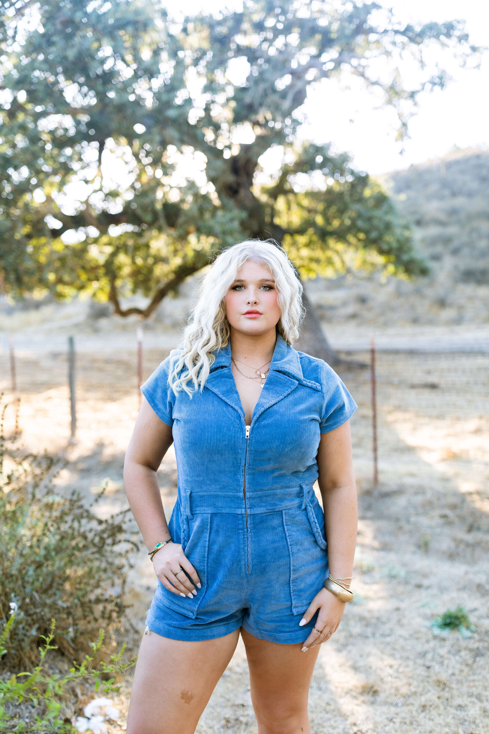blonde girl wearing blue jean romper posing in a ranch