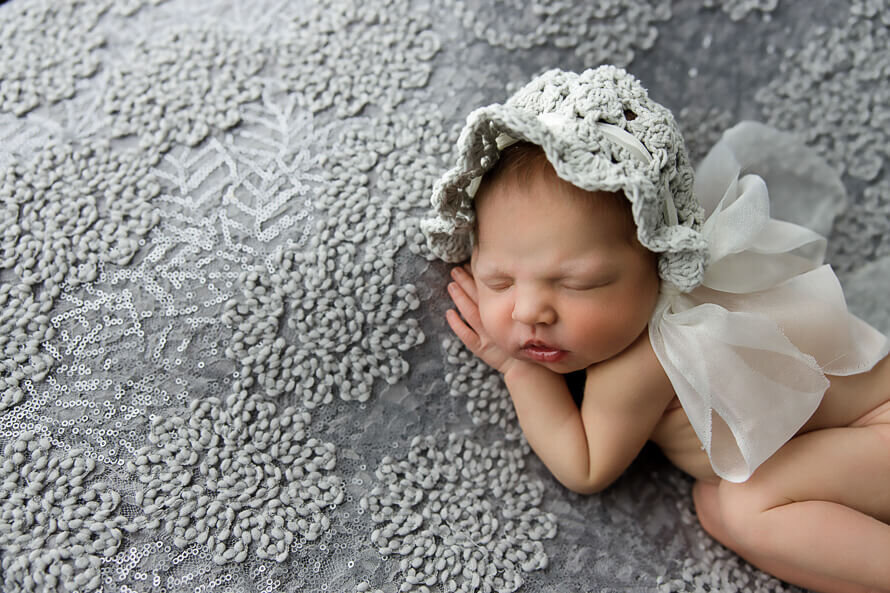 Baby girl in lace bonnet sleep on a gray backdrop.
