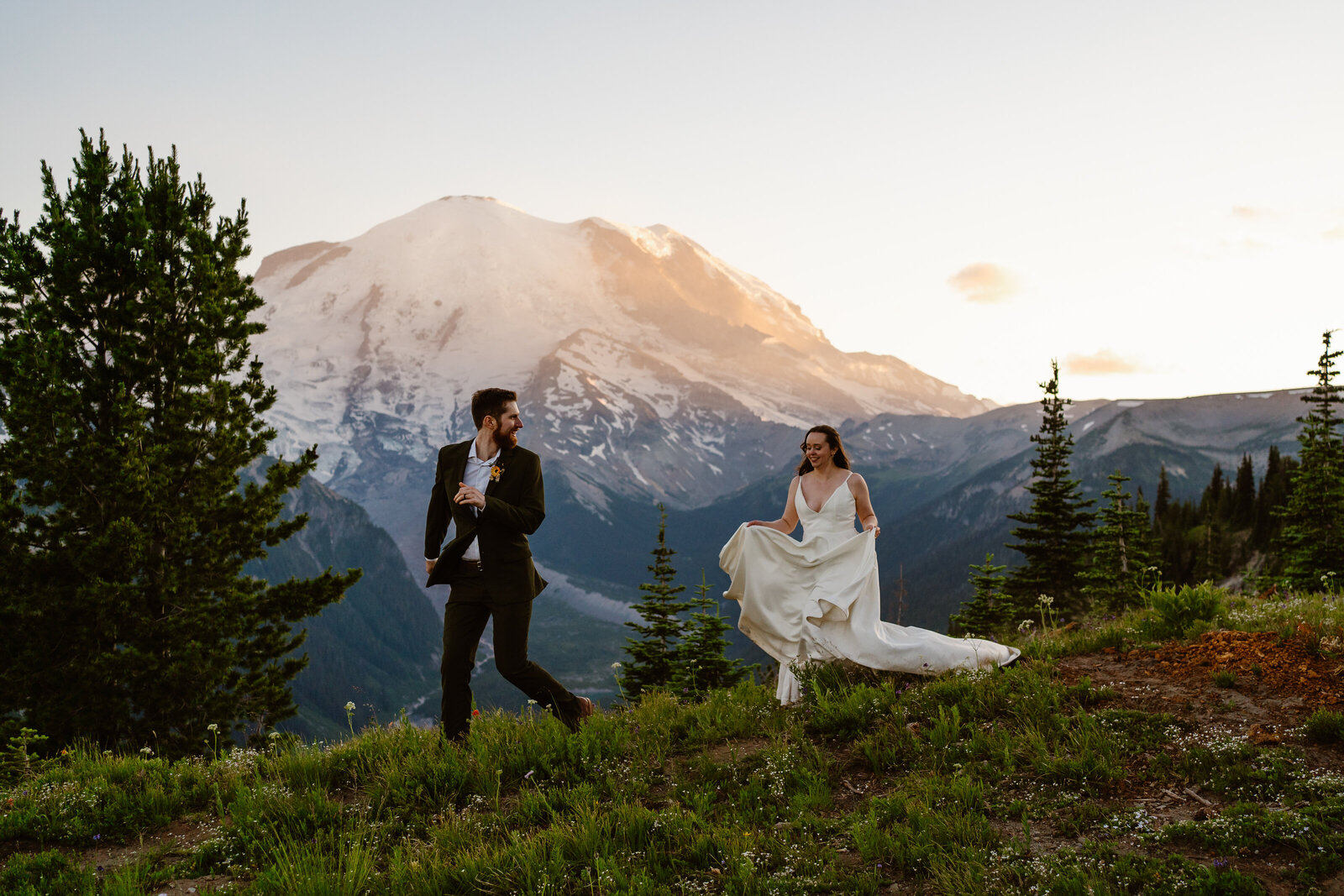 a bride and groom run together on a ridgeline overlooking Mount Rainier during their Washington elopement