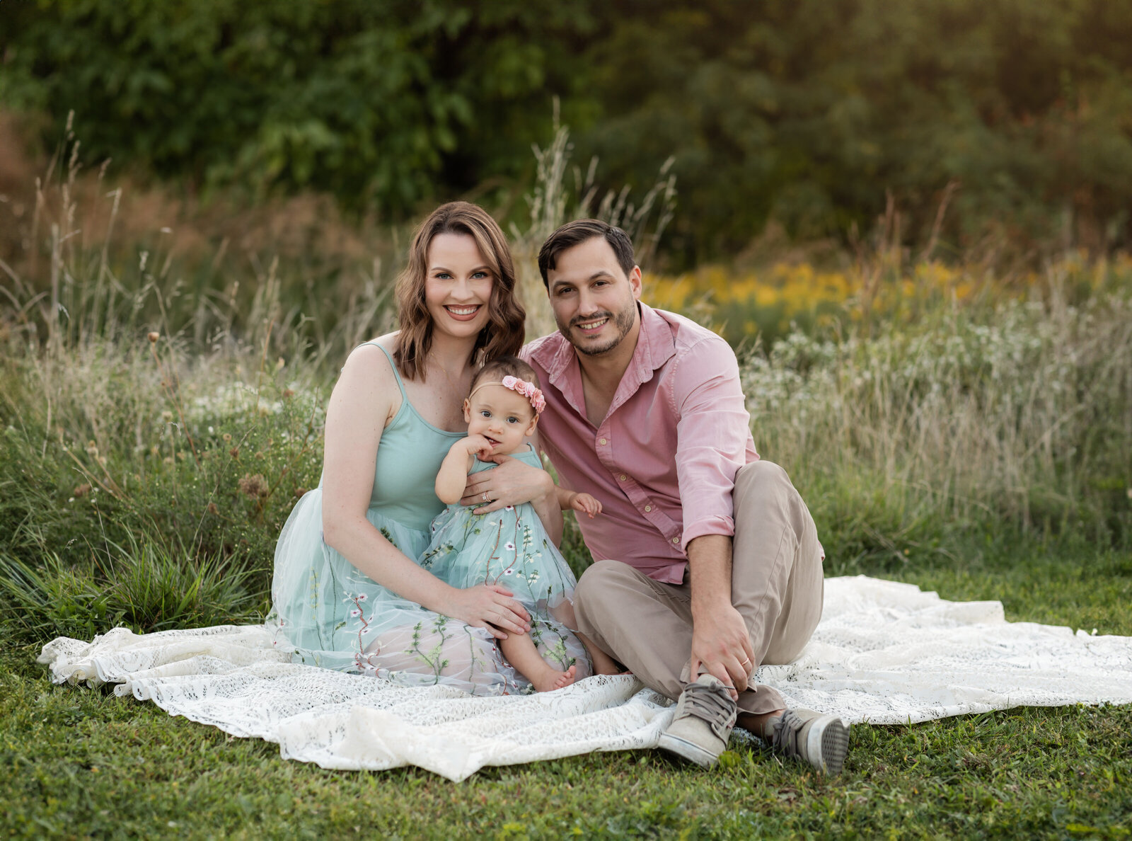 mom and dad sitting in park holding one year old daughter for family photos