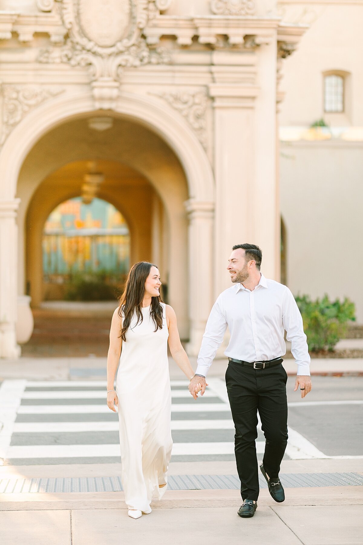 Engaged couple walking holding hands together across the street during their engagement photography session in Balboa Park.