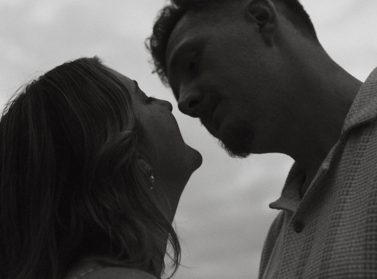 A couple going in for a kiss beside a lake, captured in a documentary style.