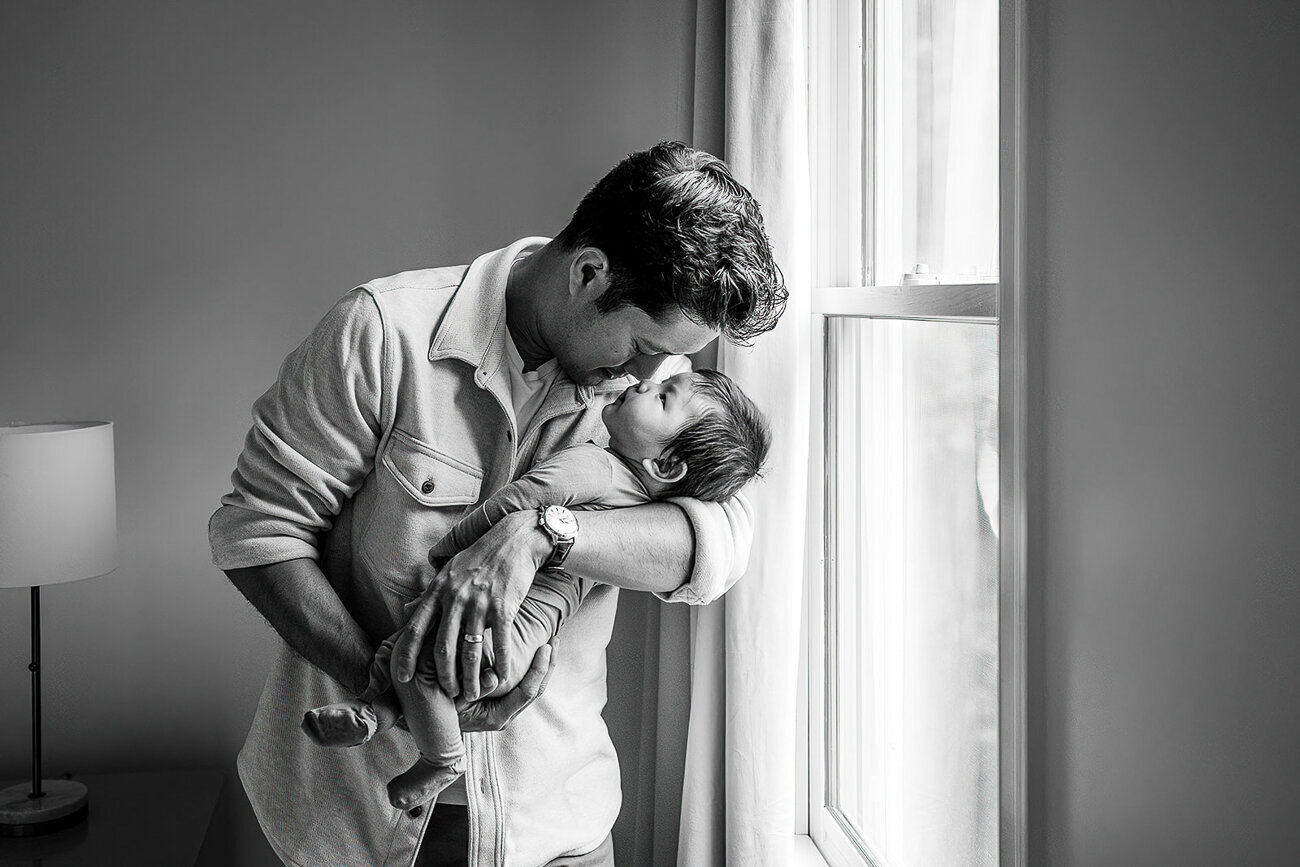 black and white portrait of dad and newborn at window