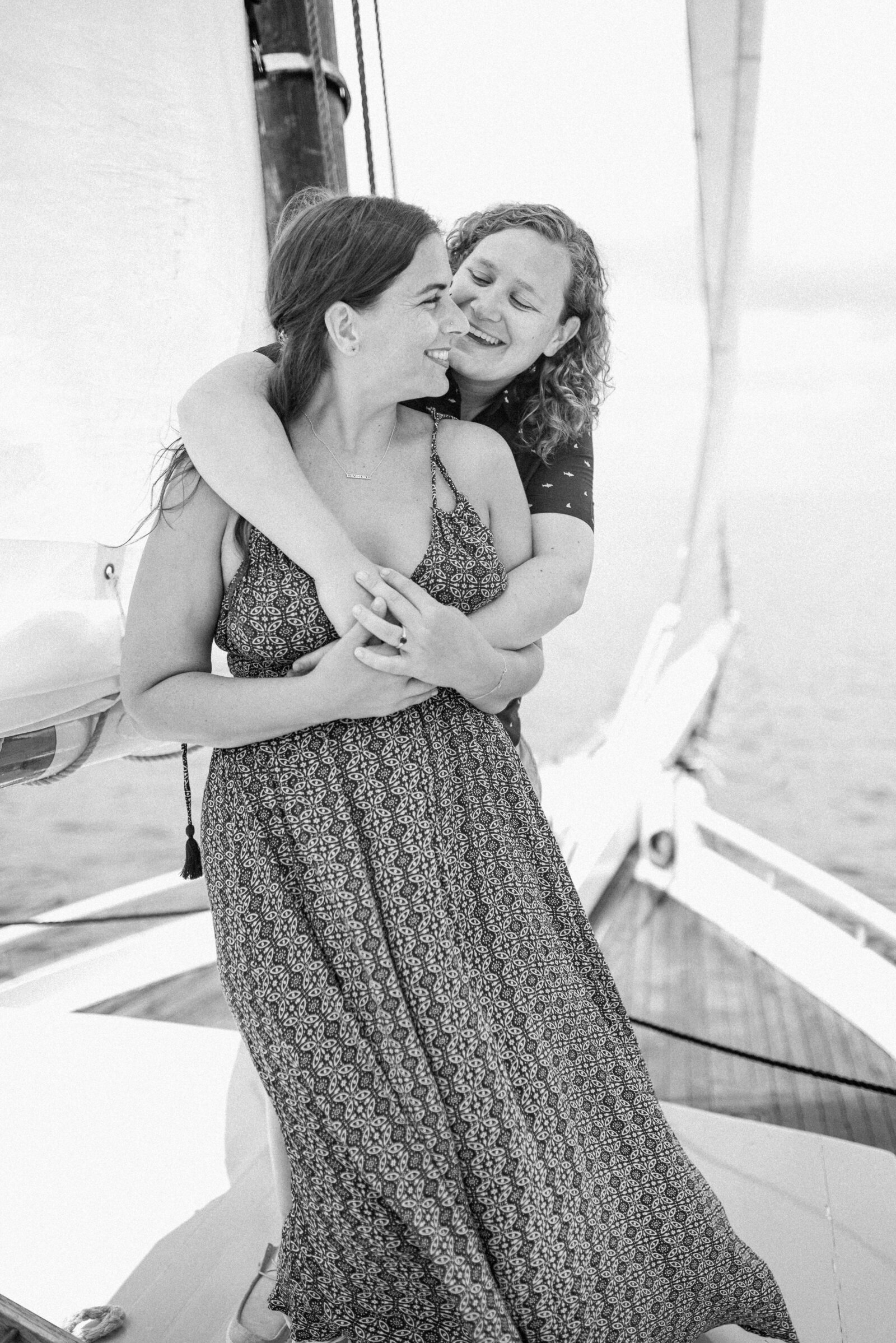 engaged couple wrapped in a from behind hug on a sailboat.