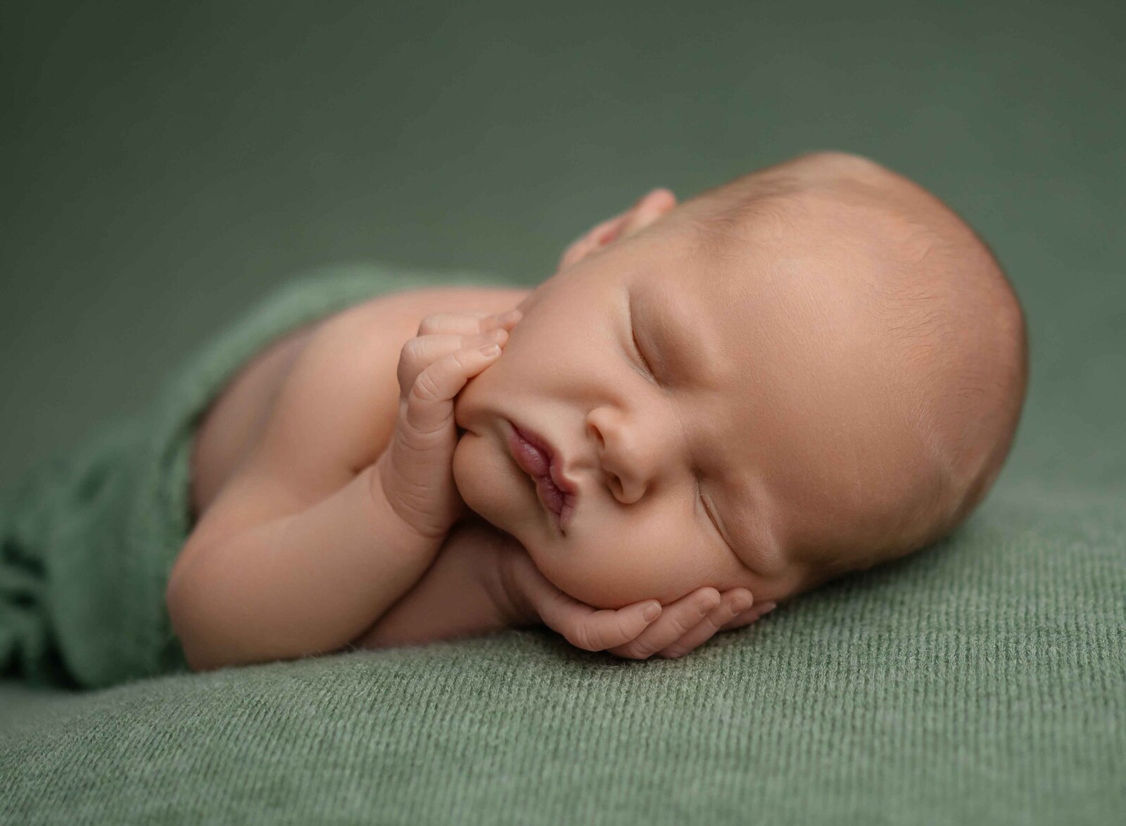 Baby boy sleeping angelically on his tummy with hands on chin. 