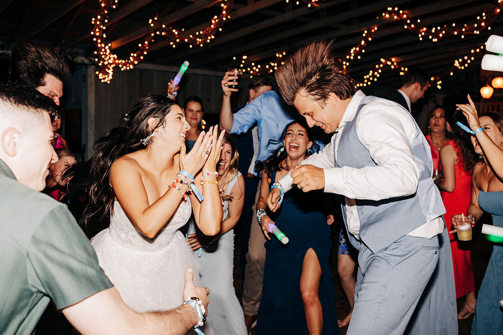 A bride and groom dance energetically at a lively wedding reception, surrounded by cheering guests under string lights, with everyone smiling and celebrating. The image was taken by a wedding photographer in Eau Claire, WI.