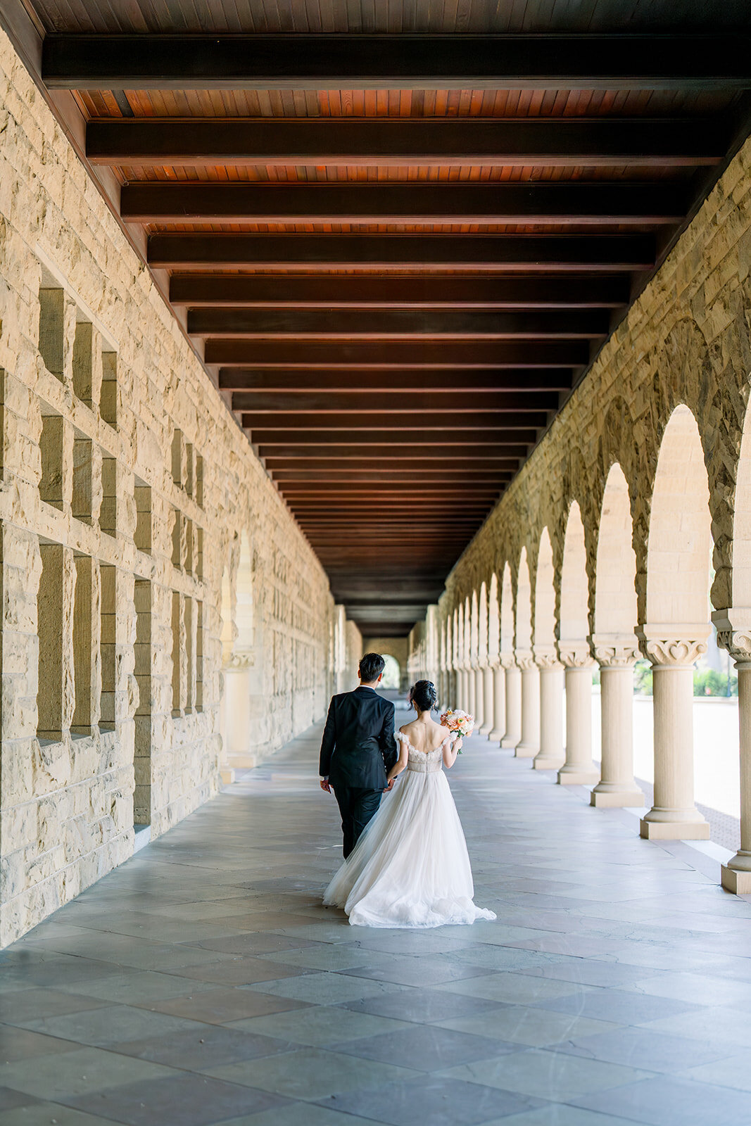 The bride and groom share a romantic moment under the iconic archway at Stanford University, epitomizing timeless love.