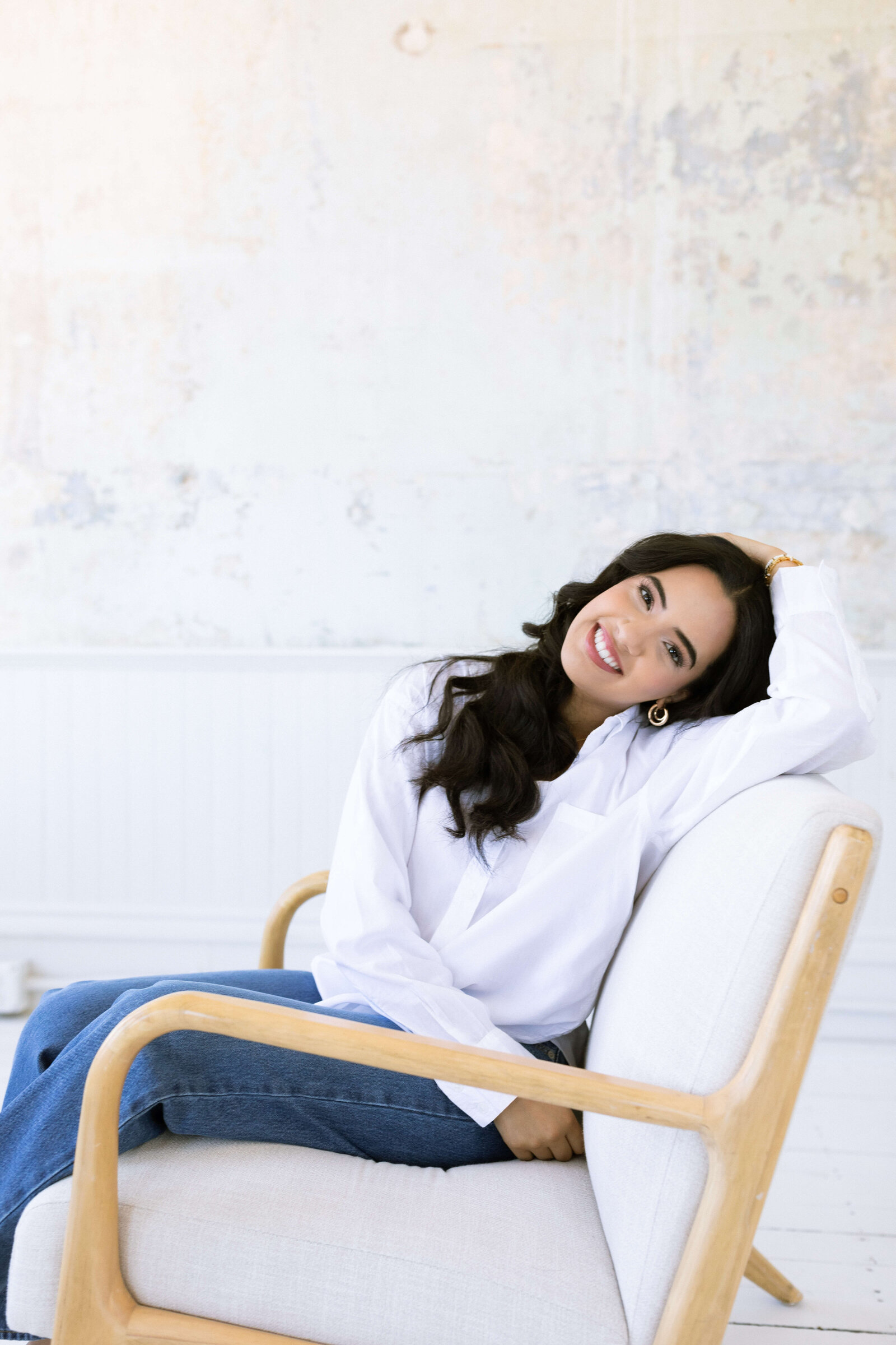 dark haired girl posing on a white and wooden chair posing for senior session