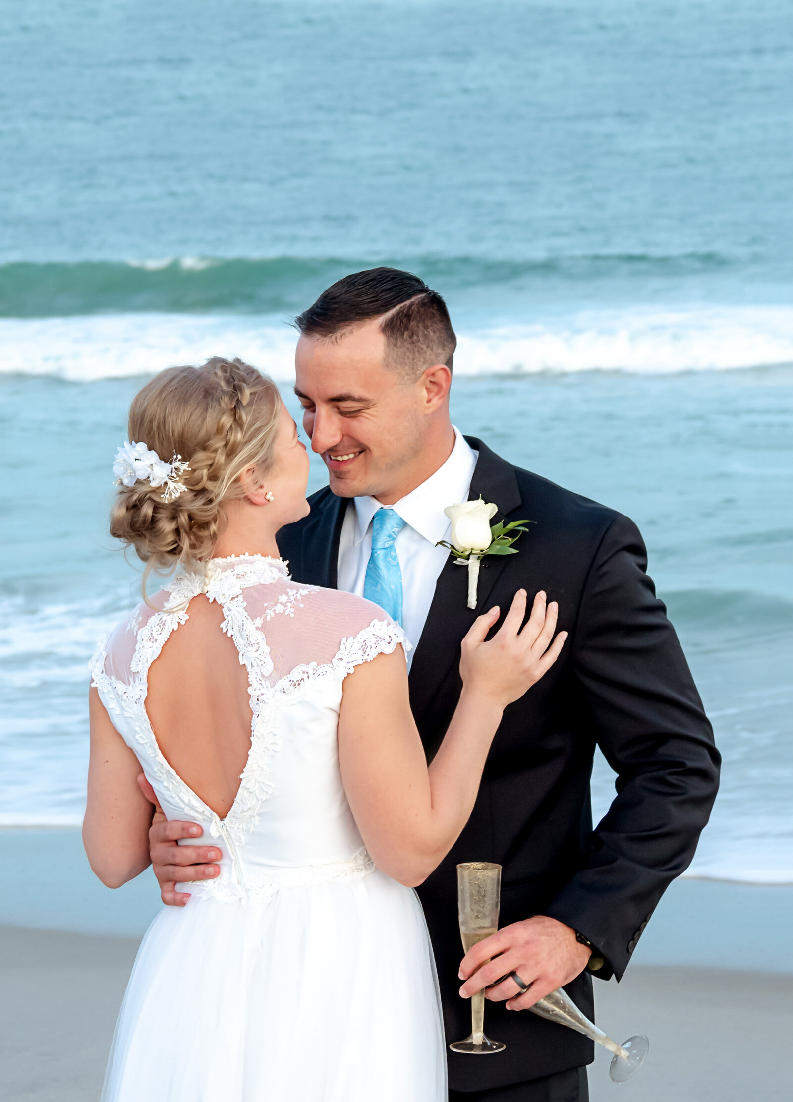 The bride and groom share a joyful moment on the beach with champagne in hand, captured during a Wrightsville Beach, NC wedding, showcasing coastal elegance and celebration.