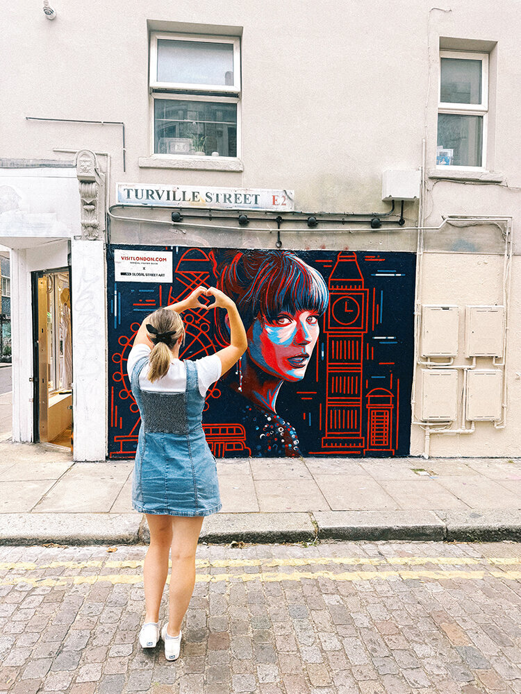 girl in front of taylor swift mural