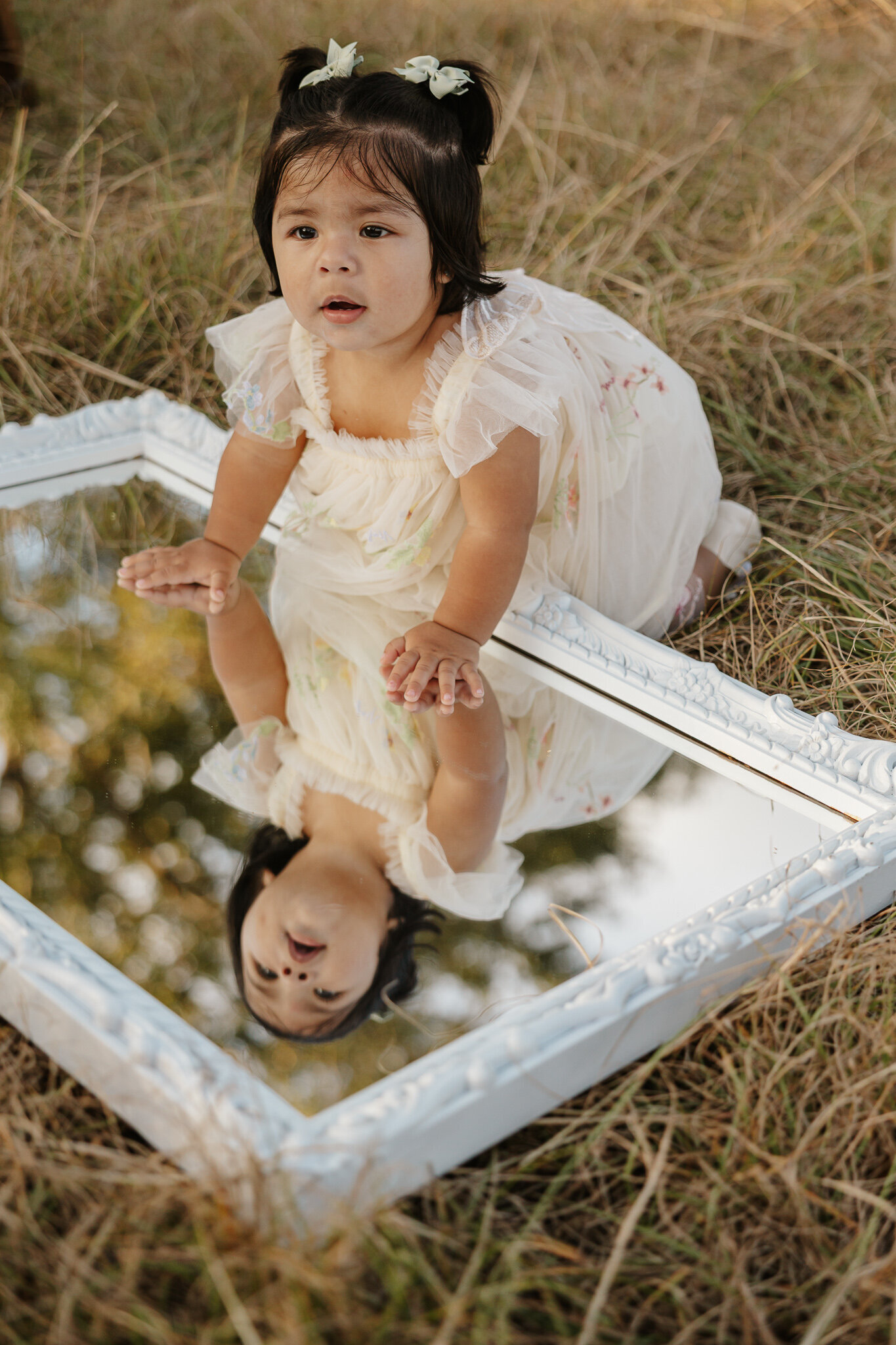 First birthday photoshoot in Aiken SC, baby girl sitting on a vintage mirror in a golden field during sunset.
