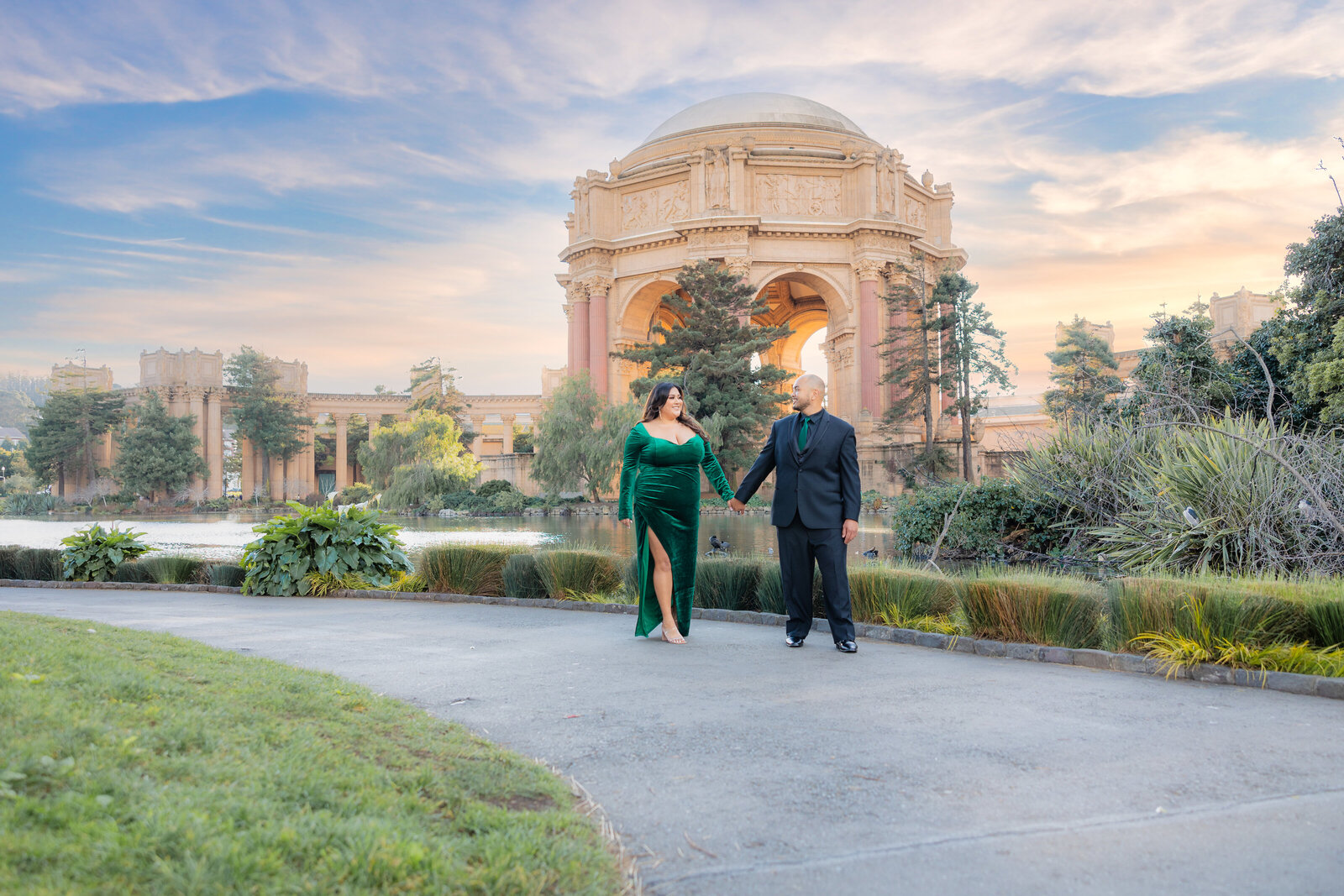 Engagement session by Philippe Studio Pro, from Sacramento, capturing a couple holding hands and walking down a  pathway at the palace of fine arts with a lake and dome in the background.
