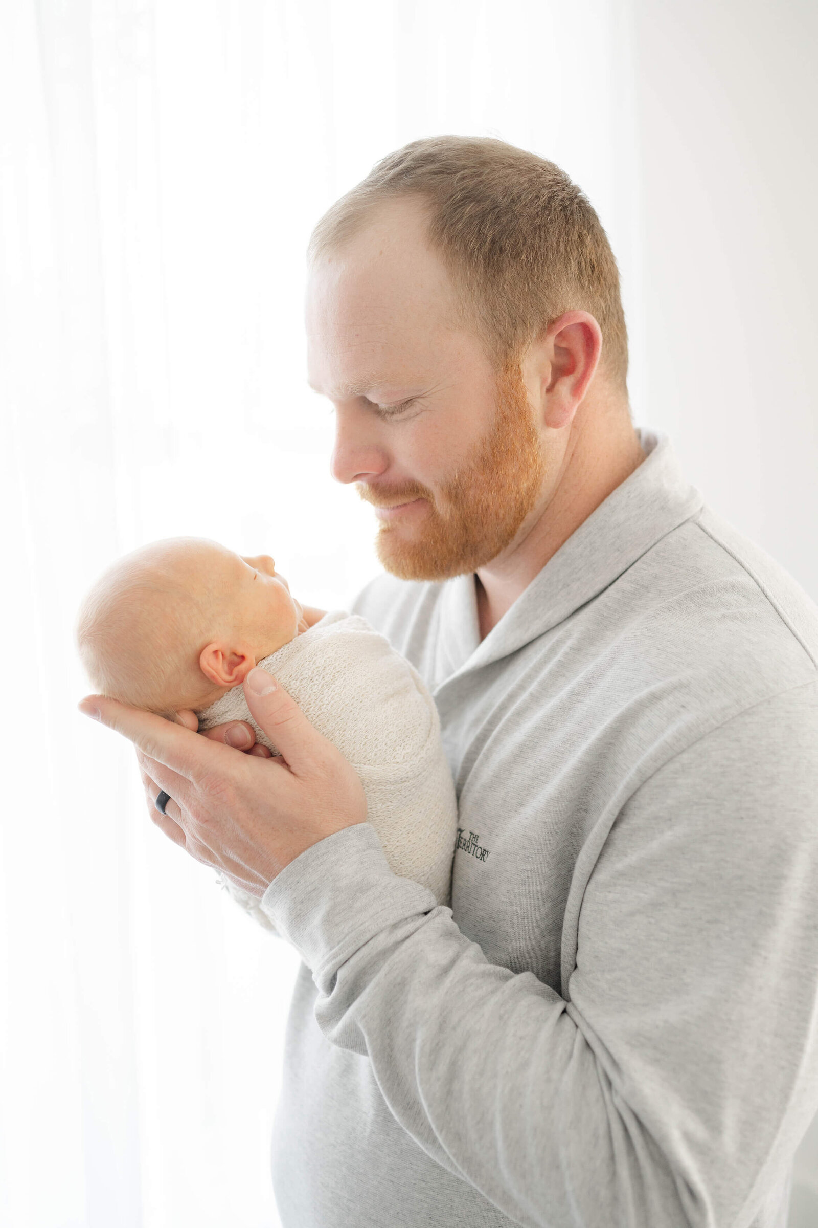 dad with a red beard proudly holds his newborn son
