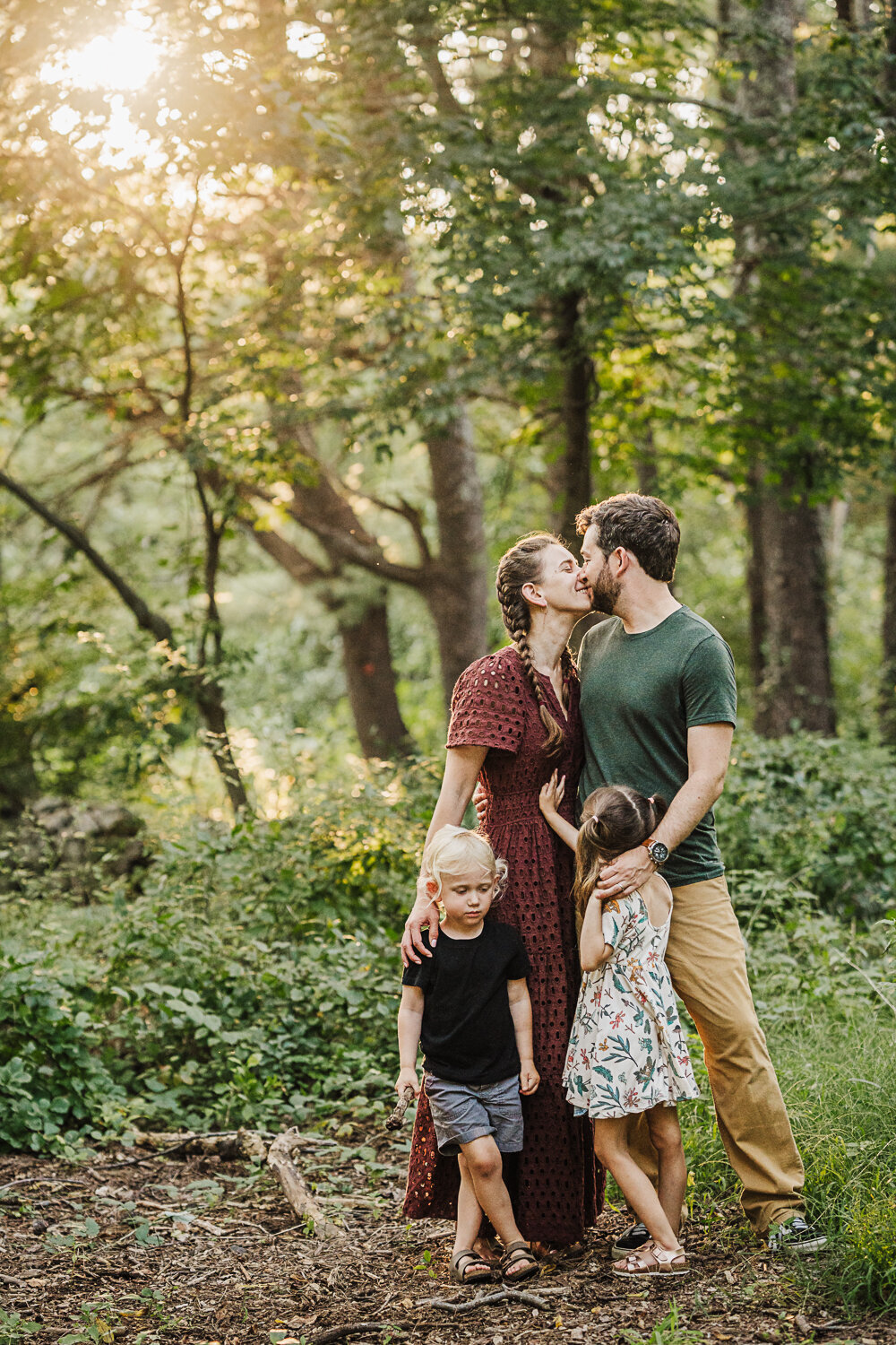 mom and dad kiss in the woods with two kids