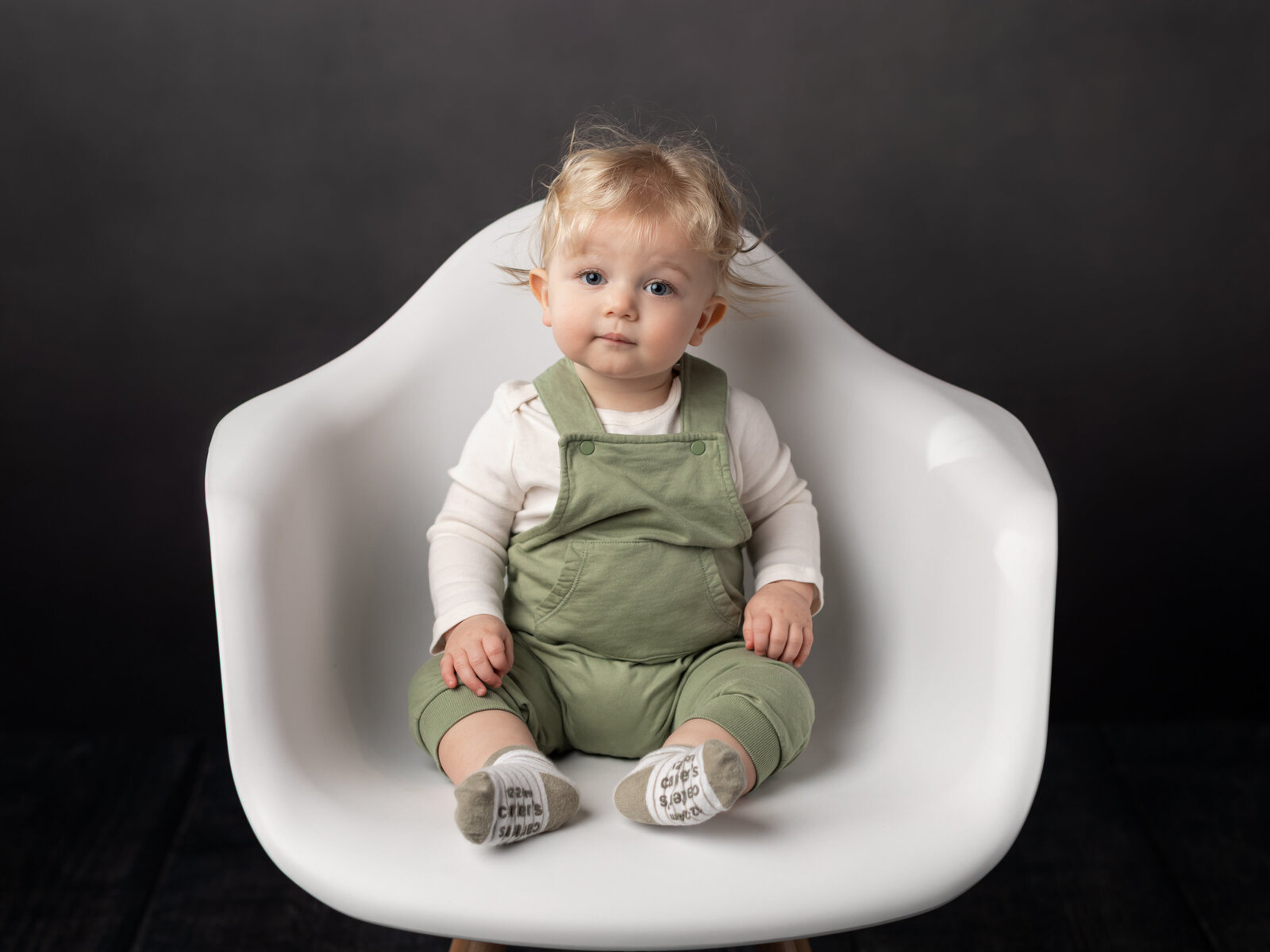 one year old boy sitting in white chair for studio portrait