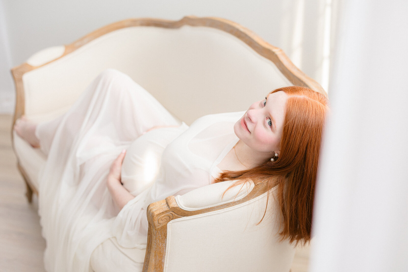 Expecting mom laying on a couch in a bright louisville maternity photo studio