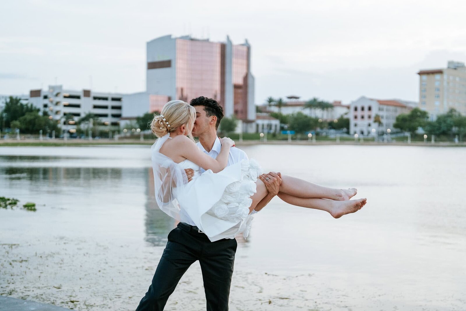 Golden hour couple portraits at Lake Mirror - Magnolia Building Wedding - groom is lifting bride, kissing her