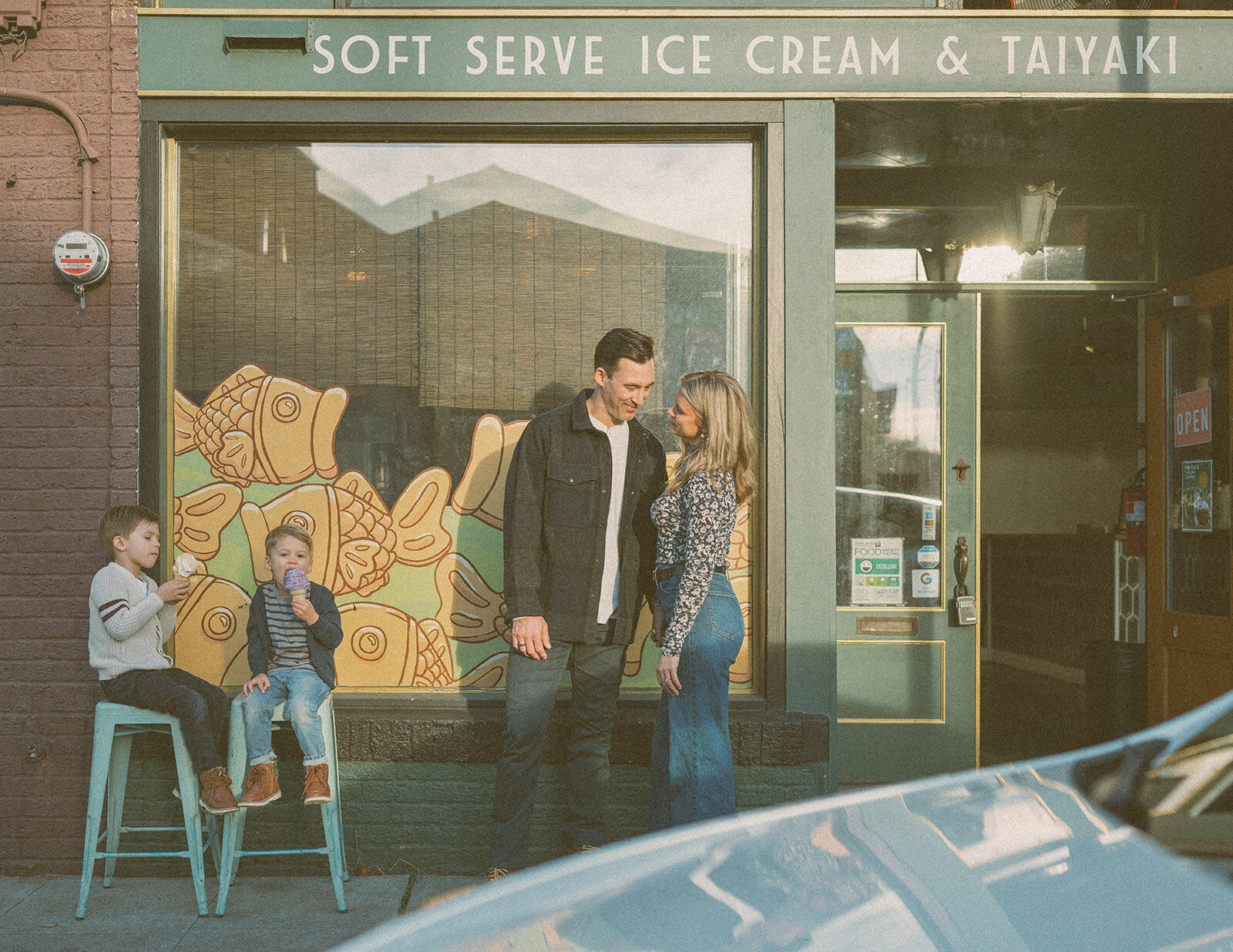 Parents standing outside a colorful ice cream shop while kids eat cones — lifestyle family photos by Orange County family photographer Maria Alcantara.