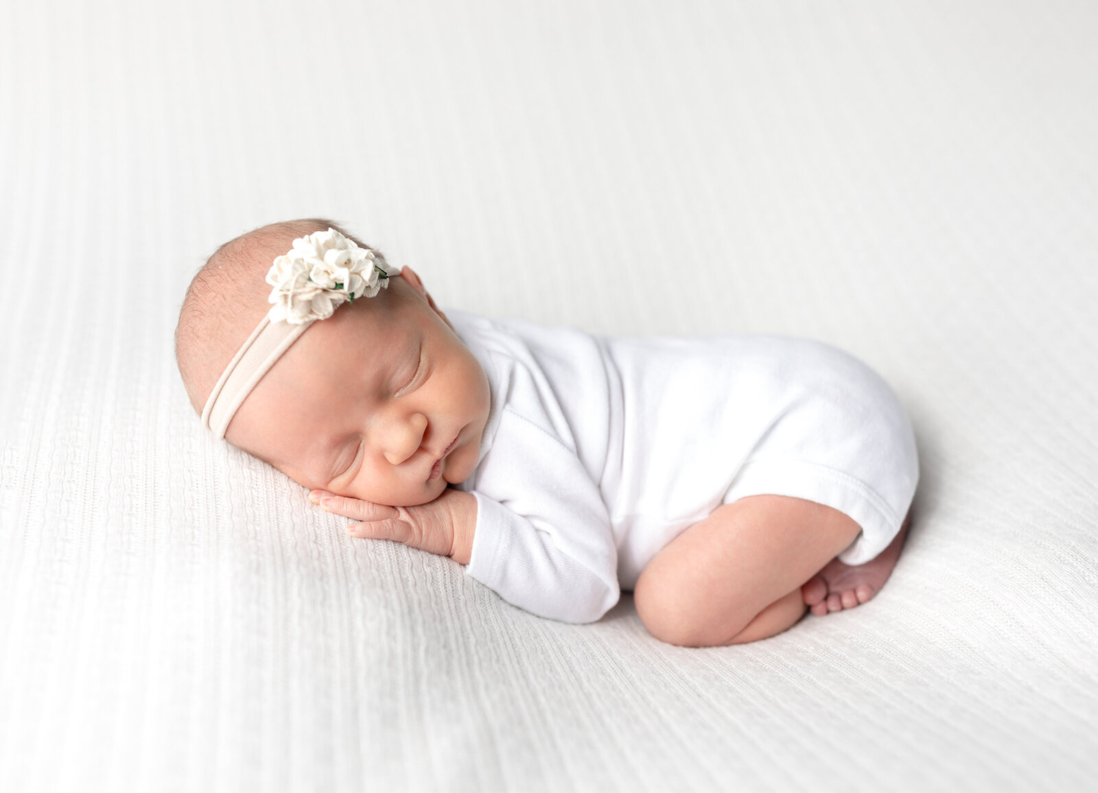 newborn baby girl posed on white fabric for newborn photoshoot