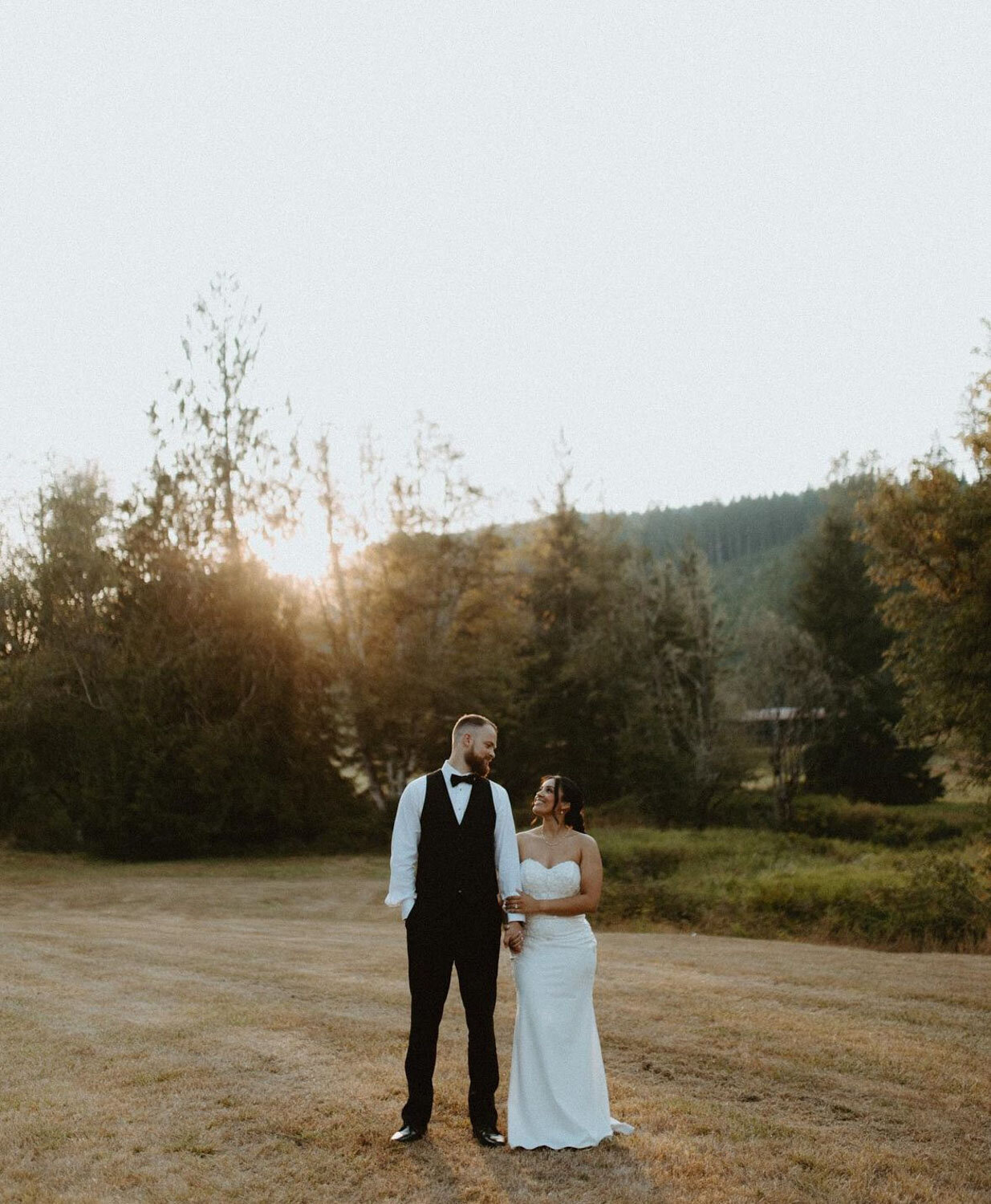 A couple standing in a golden field, soaking in the glow of the setting sun