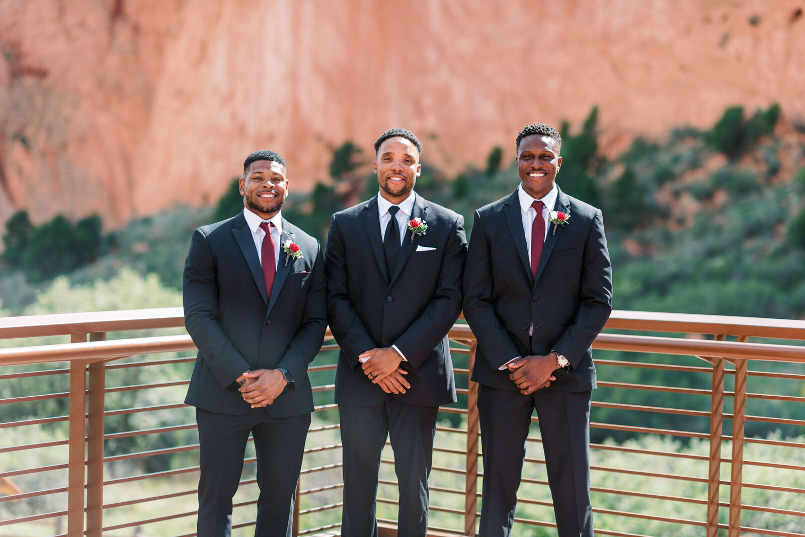 Handsome groom and his groomsmen dressed in black suits stand together and smile at the camera