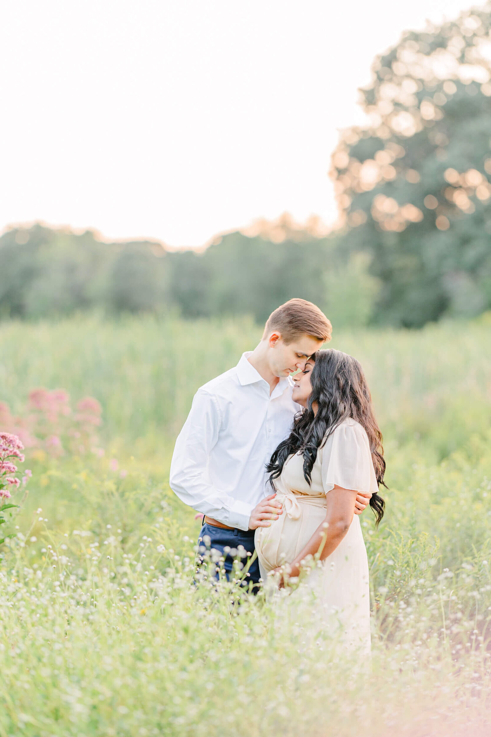 Pregnant woman leans into her husband as he places one arm around her back and the other hand on her baby bump with their foreheads touching and eyes closed