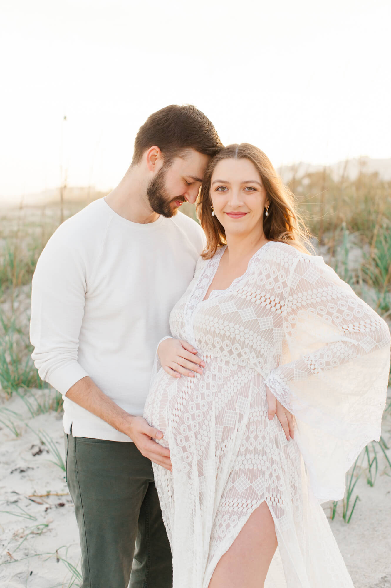 Pregnant couple posing for a photo husband holding moms belly at sunset