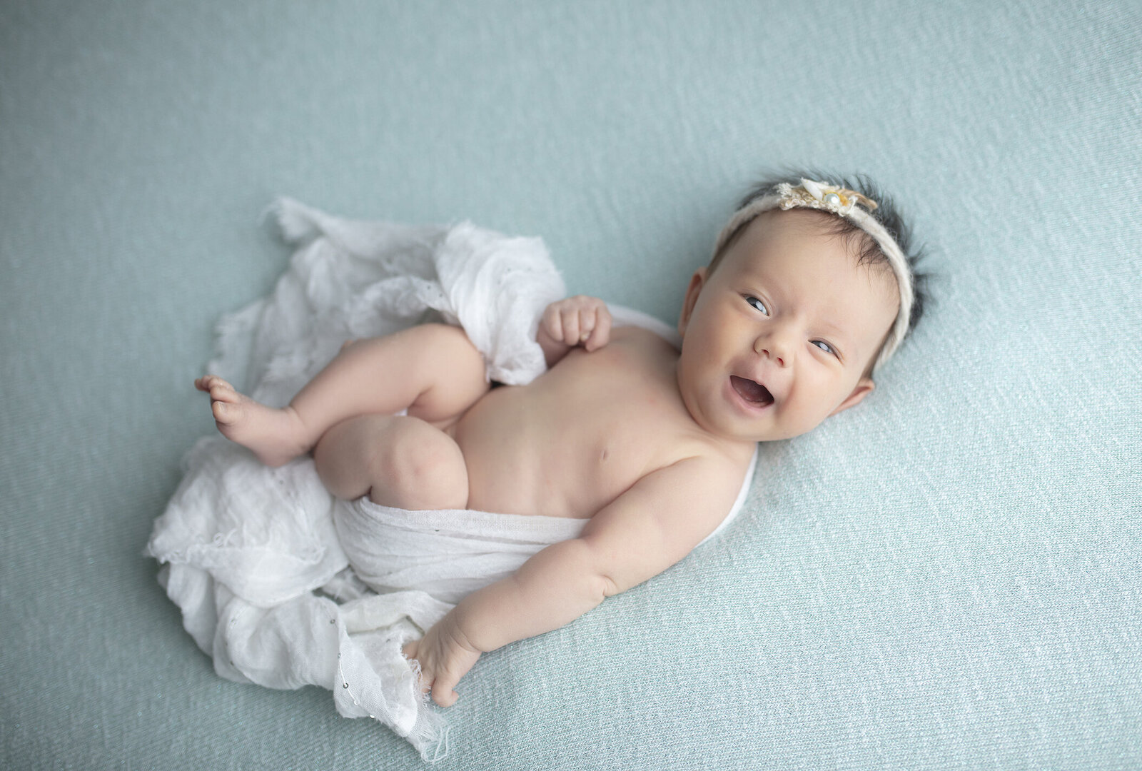 Dallas newborn girl smiling on blue fabric.