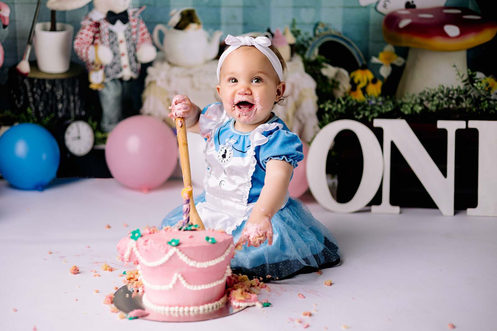Baby girl joyfully digs  in to her birthday cake with a large wooden spoon