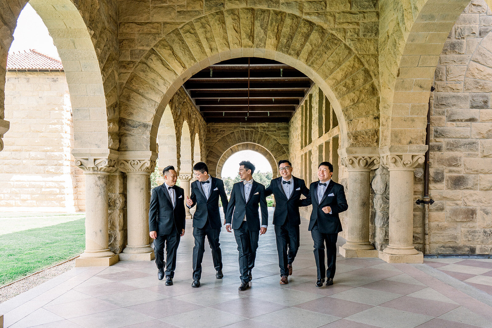 The groom and his groomsmen walk confidently through the historic arches of Stanford University, showcasing their bond and style.