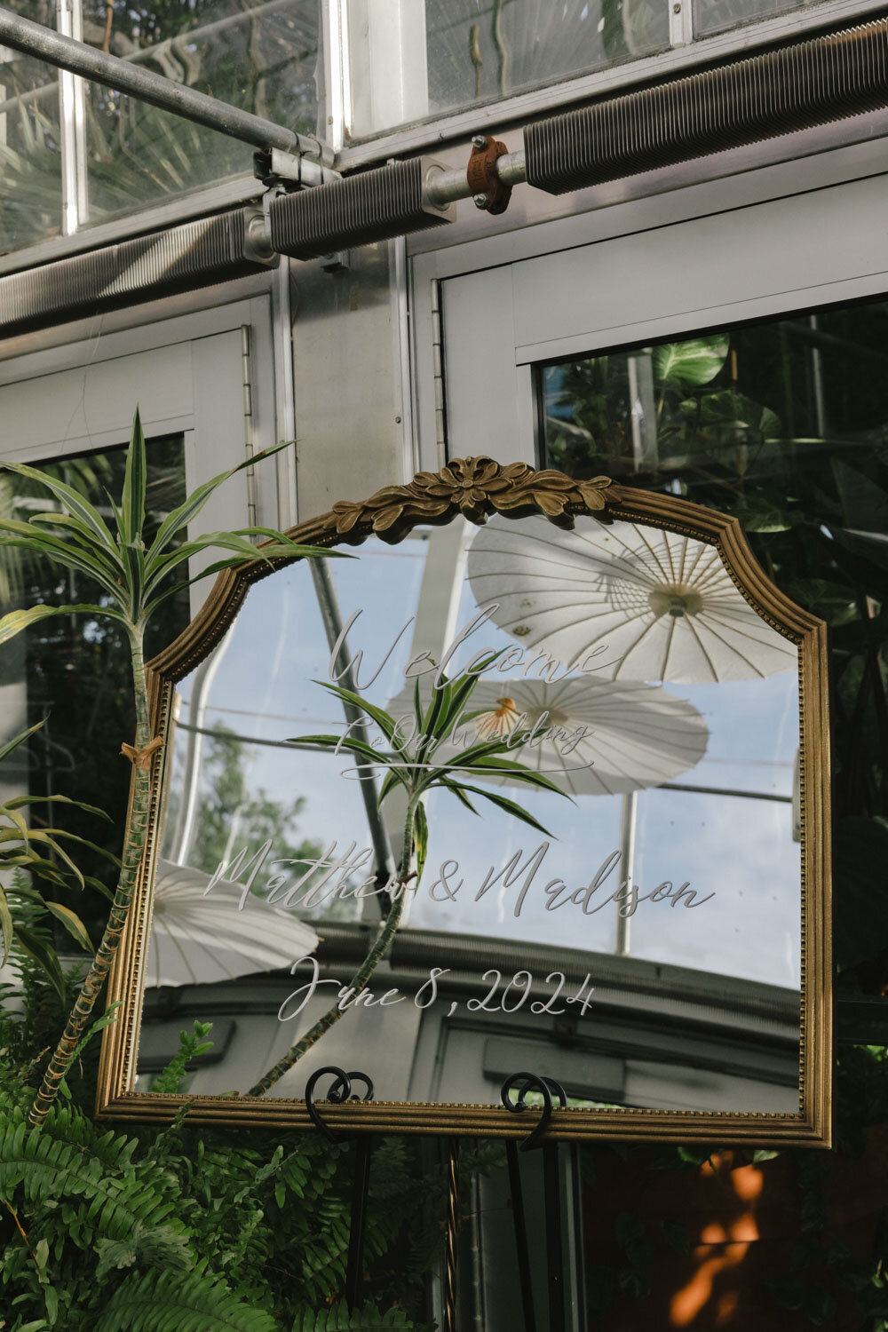 Wedding welcome sign on a decorative mirror with plants in the background