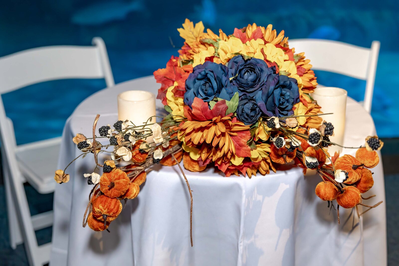 A vibrant fall wedding bouquet with blue and orange accents decorates a table with seasonal details and candles, captured during a Pine Knoll Shores Aquarium wedding in North Carolina.