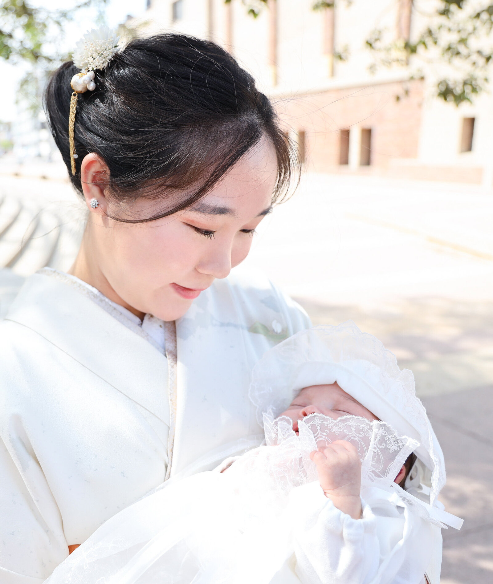 Mother in white kimono holding baby in lace bonnet for Hatsumairi celebration | 初参り 母と赤ちゃん 白い着物 ダウンタウンロサンゼルス