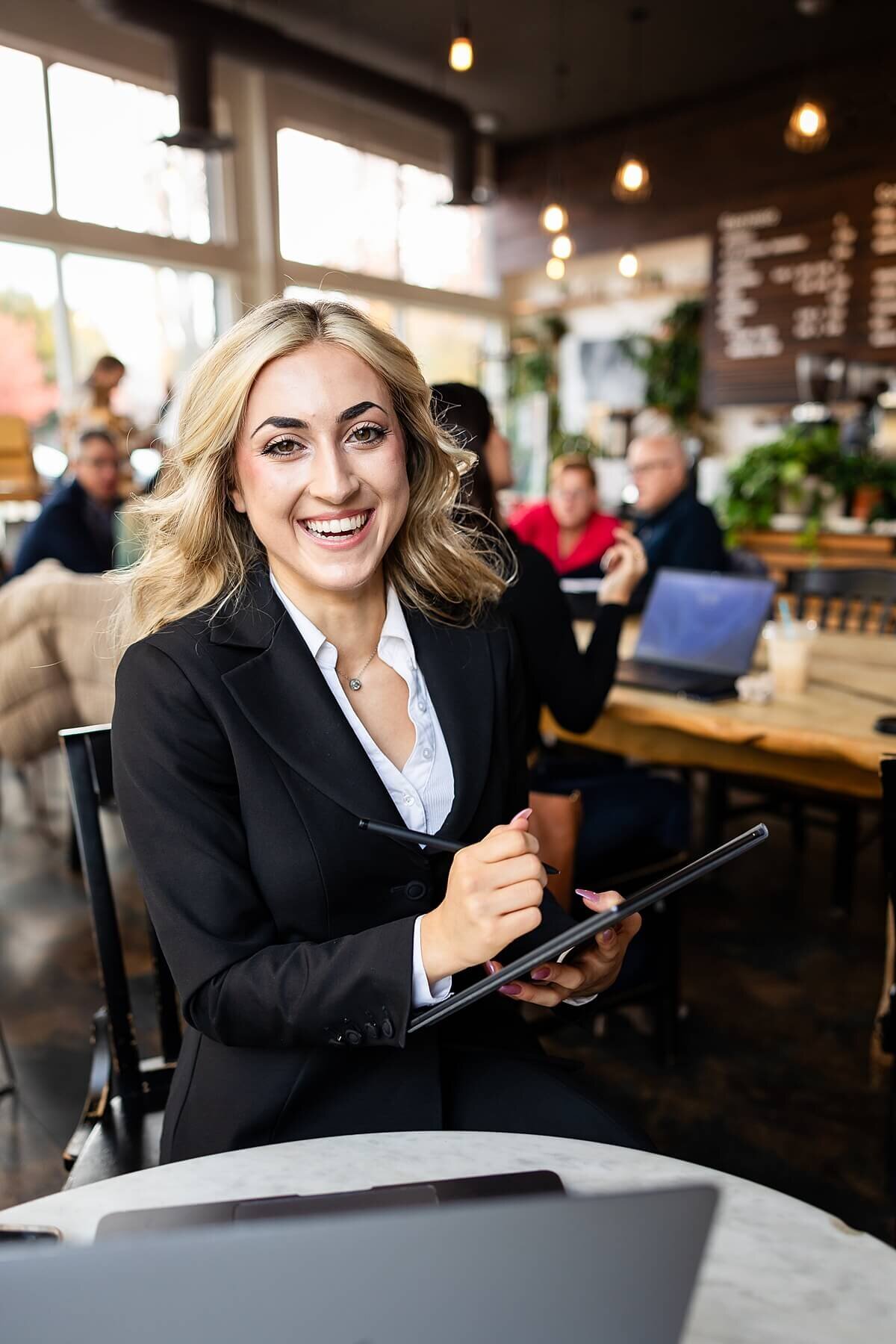 Smiling female entrepreneur writing on a tablet during a personal branding photography session in a Seattle cafe. This brand photographer near me captured a candid, professional moment that showcases approachability, confidence, and connection—ideal for modern business owners who play with fire.