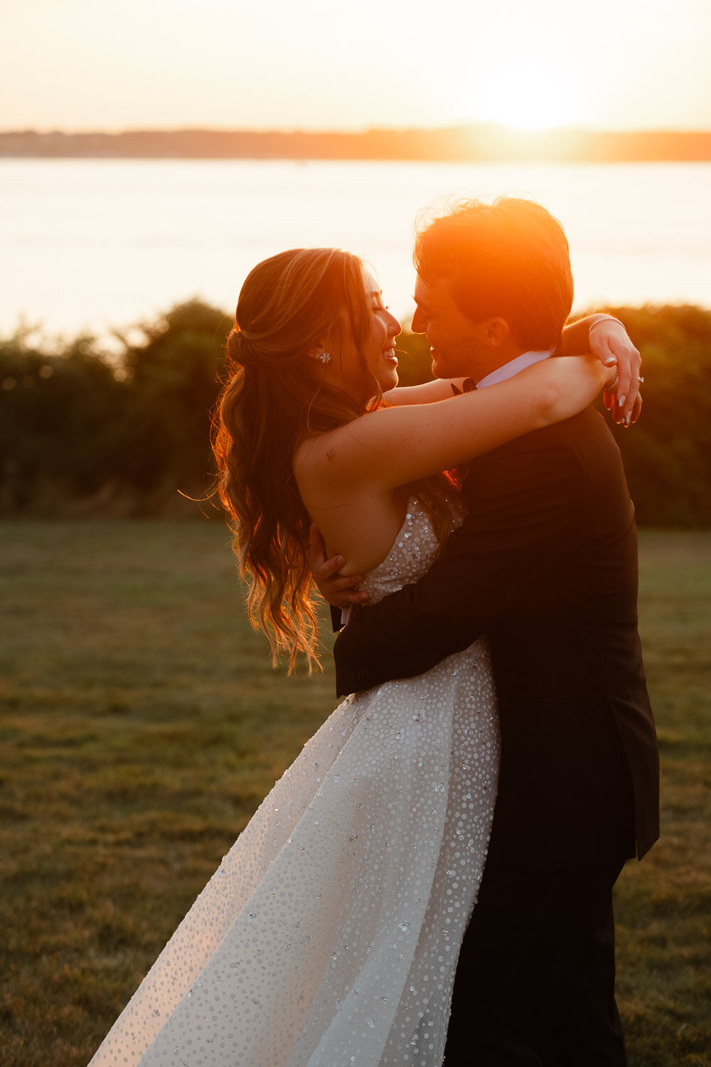 bride and groom hug at sunset by water