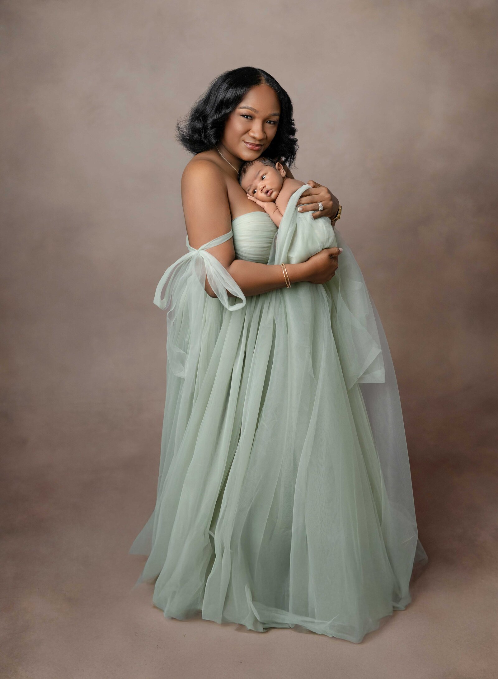 Mom in green mint tulle dress with baby snuggled on her chest. 