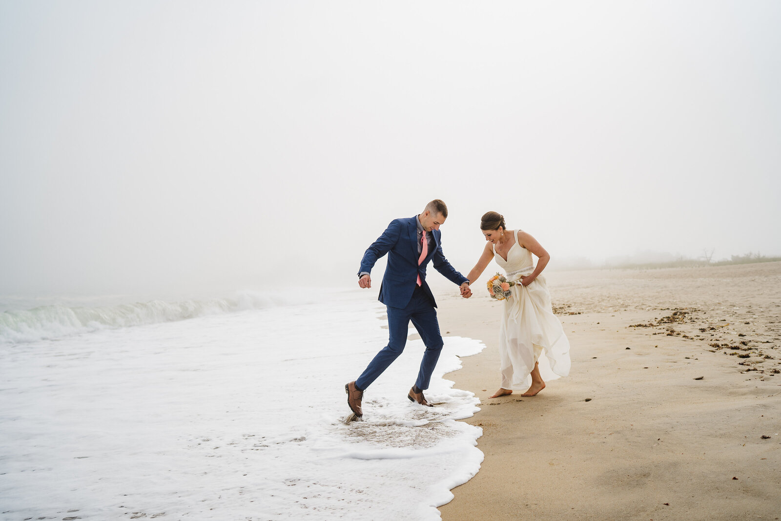 bride and groom jump to avoid a wave