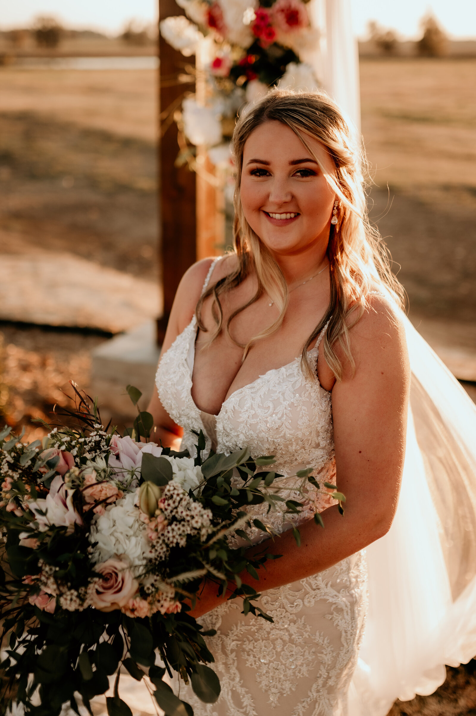 bride standing in the sun shine as the sun sets while holding her boho floral bouquet and smiles at the camera of the Best Little Rock wedding photographer