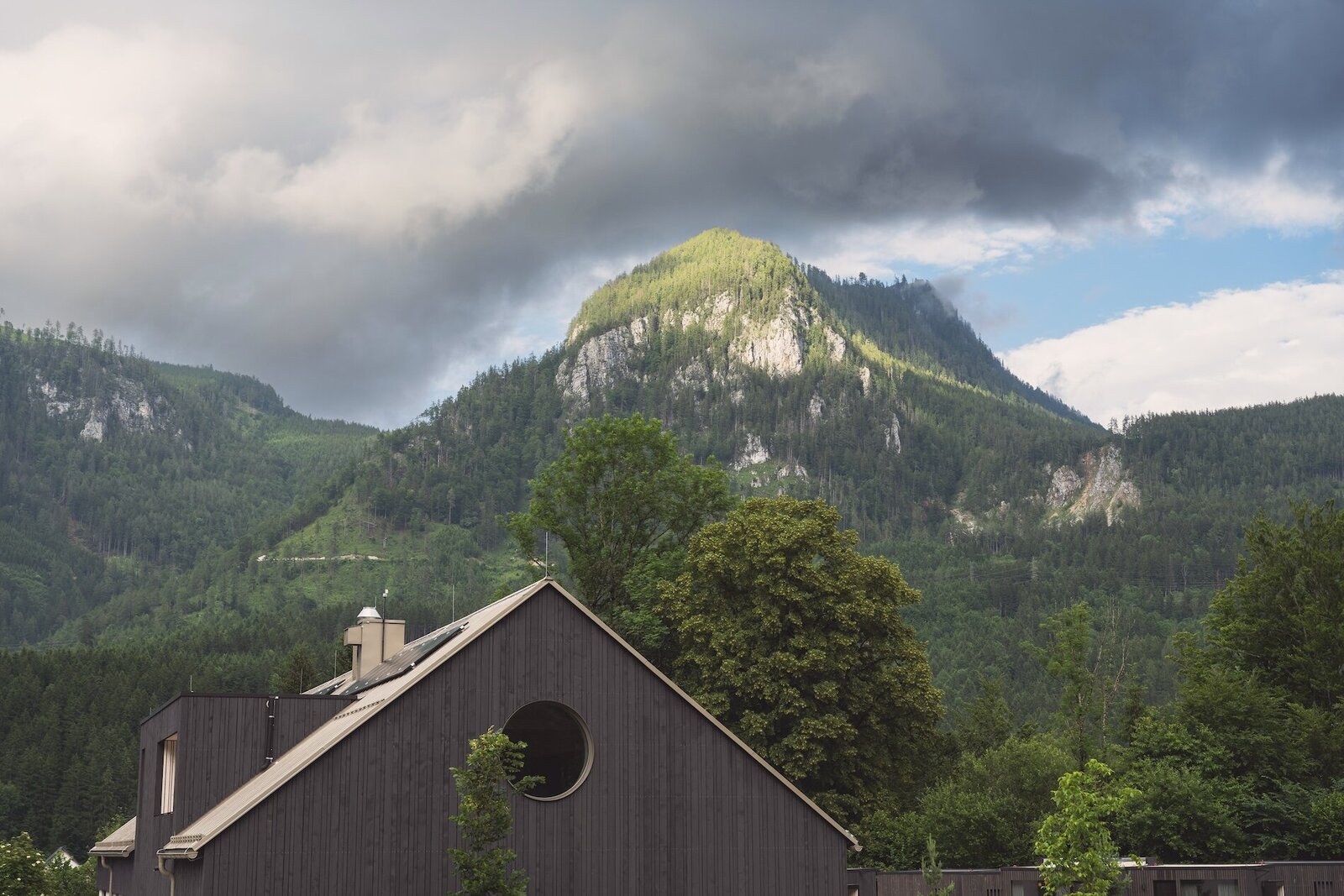 View of the top of The Campus Alps Workbase, framed by lush trees and majestic mountains, providing an inspiring setting for remote work, company retreats, and outdoor activities in the heart of the Alps.