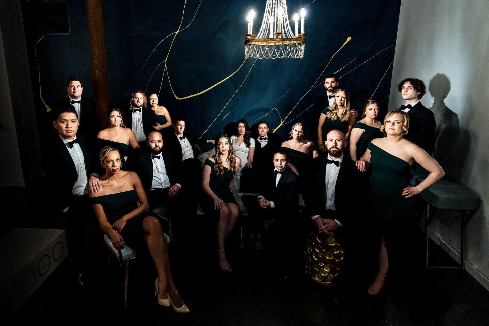 Dramatically lit group portrait of a wedding party in tuxedos and dark green dresses