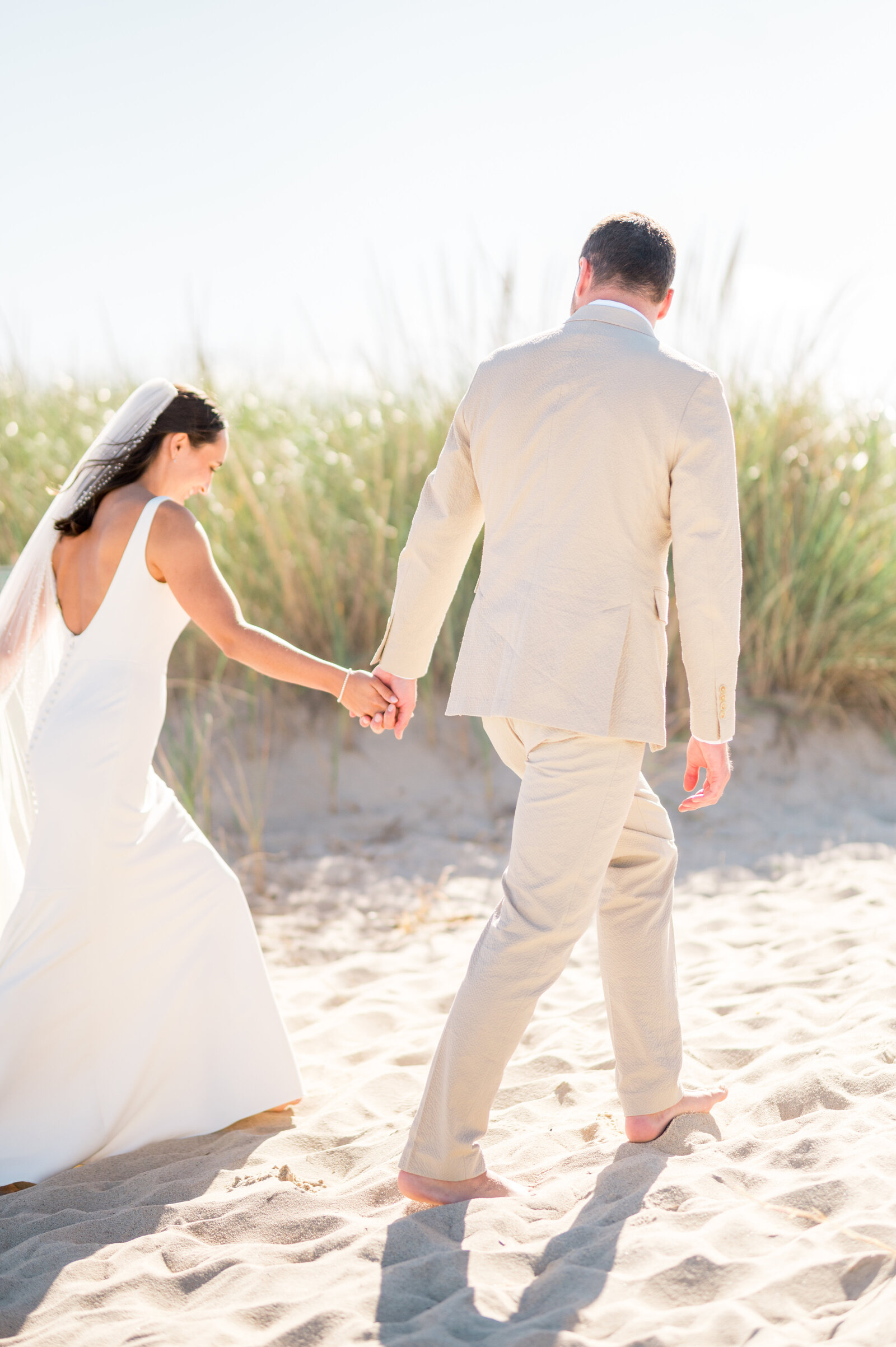Bride and groom walking hand-in-hand through beach dunes during intimate coastal Cape Cod wedding — natural, romantic photography by Sarah Surette Photography.