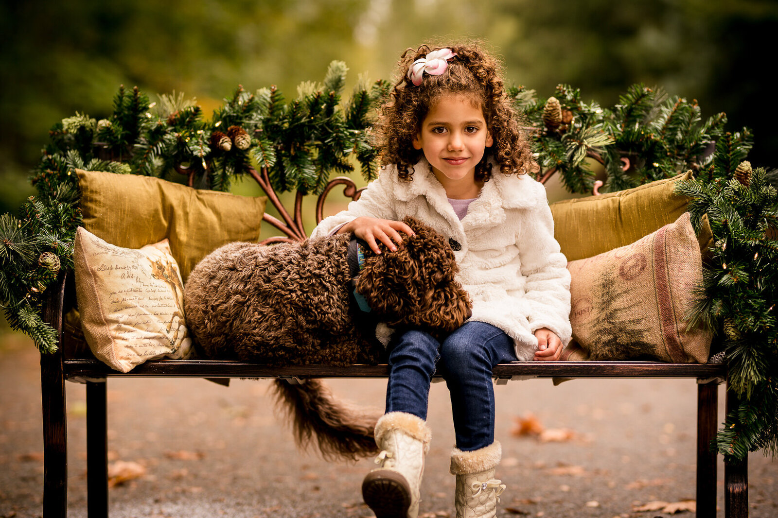 Holiday portrait of a young girl with curly hair sitting on a Christmas-decorated bench with her dog in Redmond, Washington, captured in warm golden light.